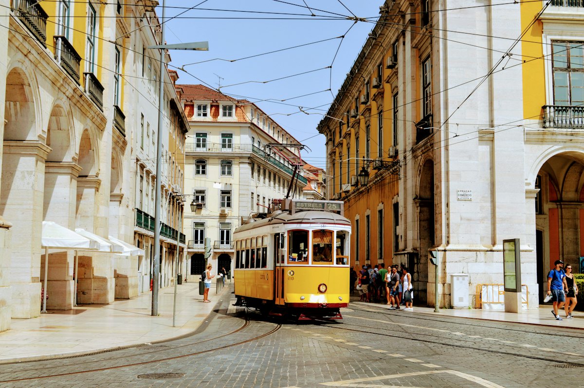 A yellow tram passing between pale stone buildings in Lisbon
