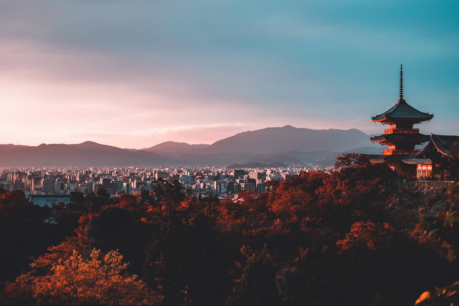A pagoda silhouetted above Kyoto at dusk with mountains beyond