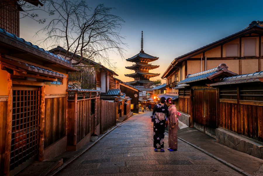 Two people in kimono walking a lantern-lit street in Kyoto's Higashiyama